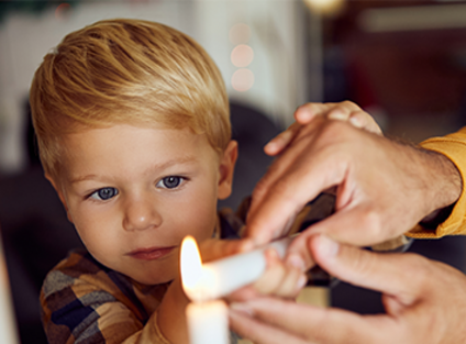 Ein Knabe zündet mit einer erwachsenen Person eine Kerze an