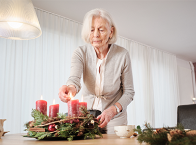 eine alte Frau zündet eine Kerze auf dem Adventskranz an