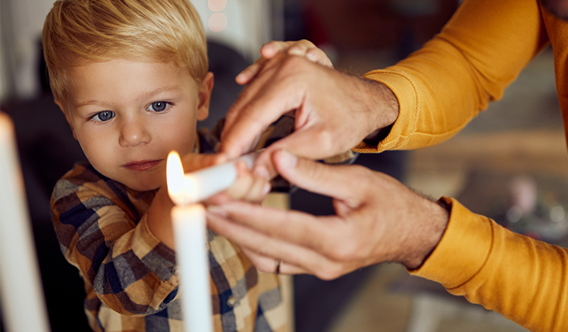 Ein Knabe zündet mit dem Vater eine Kerze an